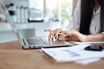 Close-up of hand businesswoman using computer laptop and smart phone working with paperwork of investment on desk