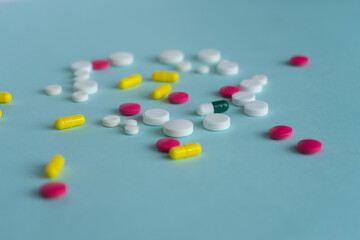 Tablets of different shapes and colors are scattered randomly. White, yellow, pink. Medical concept on blue background, pharmacy theme.
