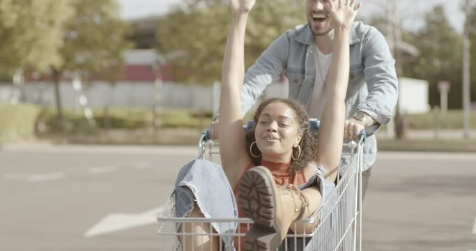 Couple playing with shopping trolley in car park and having fun together