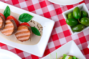 Delicious cut beef steak served on a white plate over red plaid tablecloth. Italian concept, Italian cuisine. Flat lay.