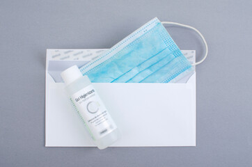 surgical mask inside a white envelope and hydroalcoolique ice jar. Gray background.