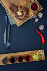 Fresh meat steak and seasonings on rustic wooden board over black background. Top view, flat lay, copy space banner.