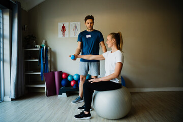 Caucasian male trainer or therapist training young Caucasian female in home gym, recovery and rehabilitation, physiotherapist