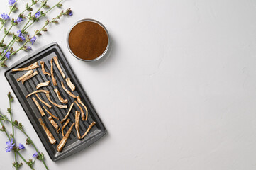 Healthly food. Dried chicory roots on a baking sheet and dry powder in a bowl. A healthy alternative to coffee. Light gray concrete background. Top view, copy space.