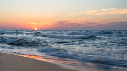 Obraz premium Beautiful sunset at the sea with rough waves on a hot, summer evening.