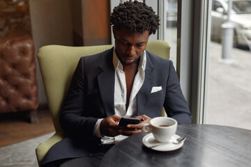 Fototapeta na wymiar Black man in a cafe. Guy drinking a coffee. Man in a black suit.