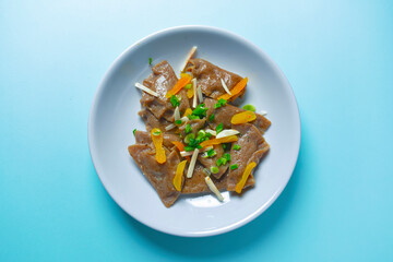 Buckwheat dumplings with greenery served on a plate over blue background. Tasty dish isolated on blue.