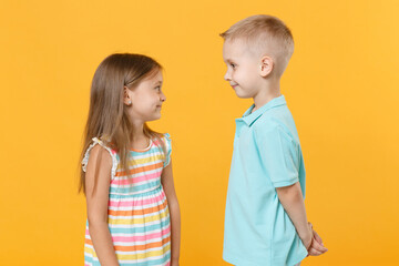 Little couple kids boy girl 5-6 years old in blue pink clothes shirt dress posing have fun isolated on yellow background children studio portrait. People childhood lifestyle concept look to each other