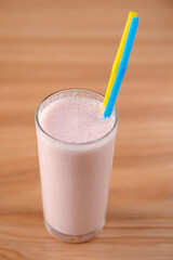Vanilla strawberry milkshake in a tall galss with two plastic straws on light rustic wooden table.