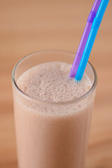 Vanilla chocolate milkshake in a tall galss with two plastic straws on light rustic wooden table.