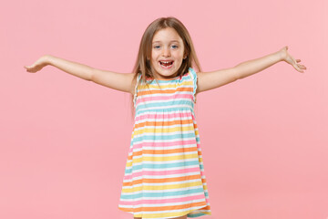 Happy little fun female kid girl 5-6 years old in colorful dress blue eyes spreading hands isolated on pink background children studio portrait. People childhood lifestyle concept. Mock up copy space