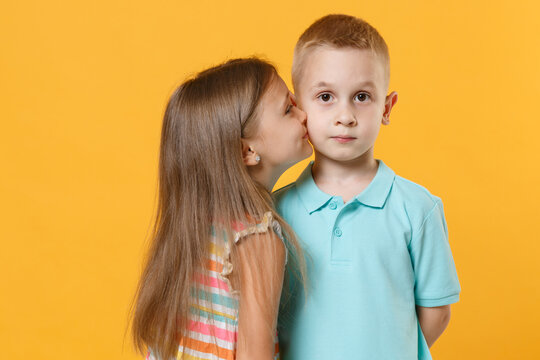 Little couple kids boy girl 5-6 years old in blue pink clothes shirt dress posing have fun isolated on yellow background children studio portrait. People childhood lifestyle concept kiss cheek love
