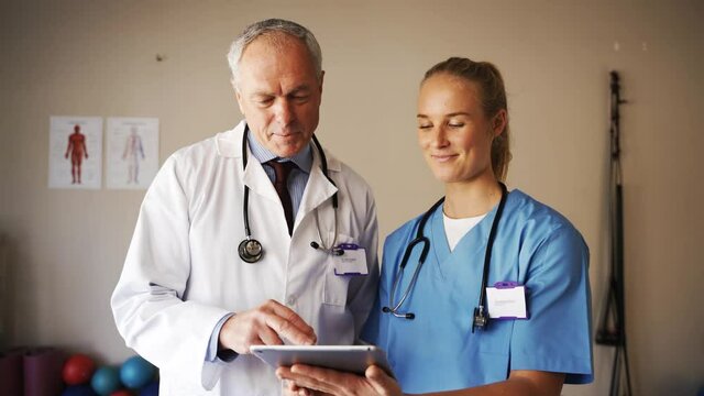 Female medical intern discussing patients diagnosis with elderly male doctor on digital tablet