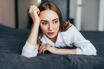 Obraz premium Thoughtful casual woman in white pajamas lying on her bed in a bright bedroom