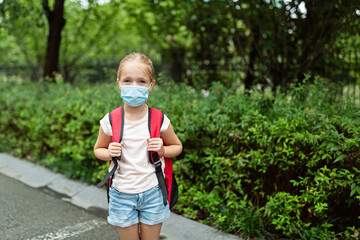 School child wearing face mask during coronavirus pandemic outbreak. Blonde girl going back to school after covid-19 quarantine and lockdown. Kid in medical mask for coronavirus prevention. New normal