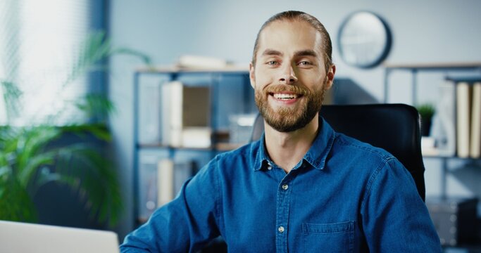 Close up of cheerful handsome Caucasian man putting off medical mask and smiling to camera while sitting at office. Happy male employee in good mood in cabinet indoors. Portrait concept
