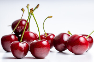 group of red and dark red cherries with green stems top facing, three cherries are in focus, on white and light grey background, soft reflections