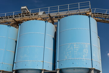 Big blue metallic Industrial silos for the production of cement at an industrial cement plant on the background of blue sky.