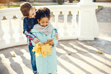 little beautiful dark-skinned girl walks in the autumn park with her European little friend