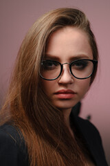Fototapeta na wymiar A young girl 20-25 years old in glasses, a jacket in the image of a teacher posing on a pink background. 