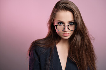 Fototapeta premium A young girl 20-25 years old in glasses, a jacket in the image of a teacher posing on a pink background. 