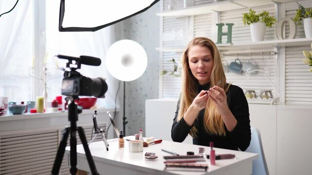 Beauty blogger woman filming daily make-up routine tutorial on camera. Influencer blonde girl live streaming eye shadow palette review in home studio with professional lighting equipment. Vlogger job.