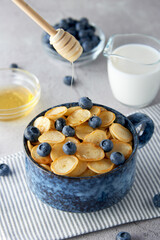 Blue Bowl of mini pancake cereal with blueberries, maple syrup and milk on concrete background. Tiny pancakes, new food trend concept. Cute healthy breakfast or snack. Recipe, menu.