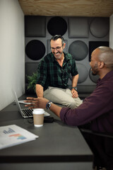 Two smiling businessmen working on a laptop in an office cubicle
