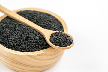Close up black sesame seed in wooden spoon and wooden bowl, spoon is on edge of wooden small bowl. Image on white background.
