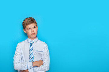 A teenage boy in a shirt and tie looks up with disbelief at the blue background. Copy space.