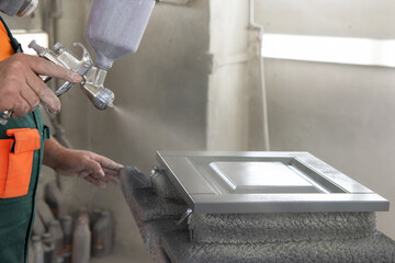 Wooden furniture production. Carpenter painting the surface of the wooden facade with a spray gun
