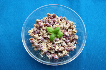 Salad with canned beans, cheese and scallops in a transparent bowl on a blue background