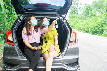 two happy Asian woman wearing protective mask sitting on hatchback car hand holding coffee cup travel with new normal lifestyle 