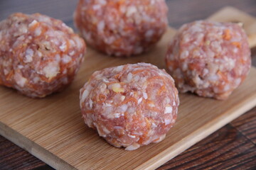 Raw minced meat meatballs with rice and carrots on a wooden Board, side view close