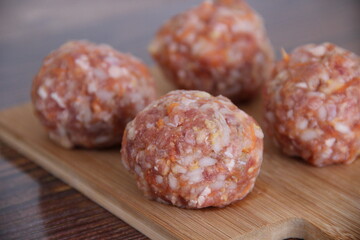 Raw minced meat meatballs with rice and carrots on a wooden Board, side view close