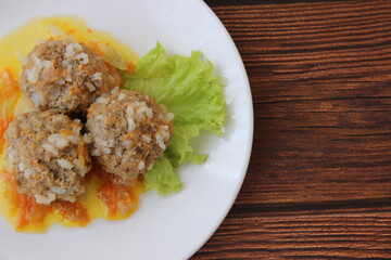 Meatballs with rice and carrots on a white plate and dark wooden boards