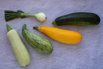 several types mixed yellow, white, stripped and green zucchini's and onion on a grey concrete background. top view, copy space