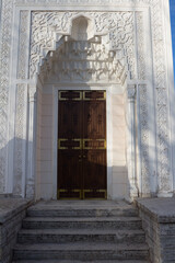 A brown wooden door inside a white carved wall is the entrance To the pavilion