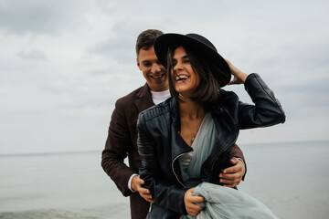 Cheerful smiling couple in love hugging at sea shore. Beautiful  stylish couple having fun on the beach. People, love, happiness, travel and lifestyle concept.