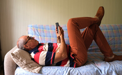 a man lies on a sofa holding a smartphone in his hands