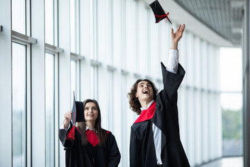 Man and woman graduates throwing graduation hats in the air. Happy couple of students in the graduation day are throwing graduation hats and holding certification in hand