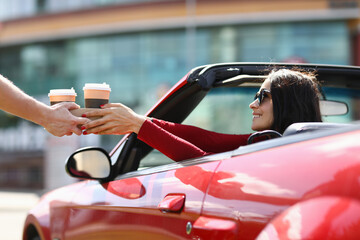 Woman in cabriolet picks up hot drinks from a courier. Food and drink delivery concept