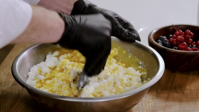 Men's hands in black gloves stir curd cheese and the yolk eggs in a bowl. 4K