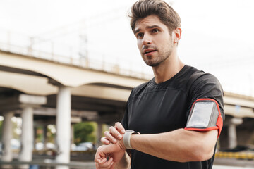 Image of athletic young sportsman using smartwatch while working out