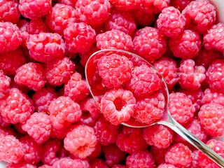 Juicy ripe raspberries are selected with a silver spoon. Natural berry background.
