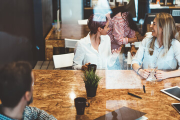 Group of young women joking with each other enjoying work break together sitting at table,positive...