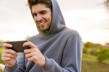 Fototapeta premium Image of athletic smiling sportsman playing video game on cellphone