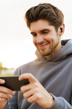 Image of smiling man with earphones playing video game on cellphone