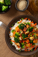 Tofu with rice and vegetables. Served on brown plate with chopsticks. Top view.