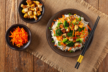 Tofu with rice and vegetables. Served on brown plate with chopsticks. Top view.